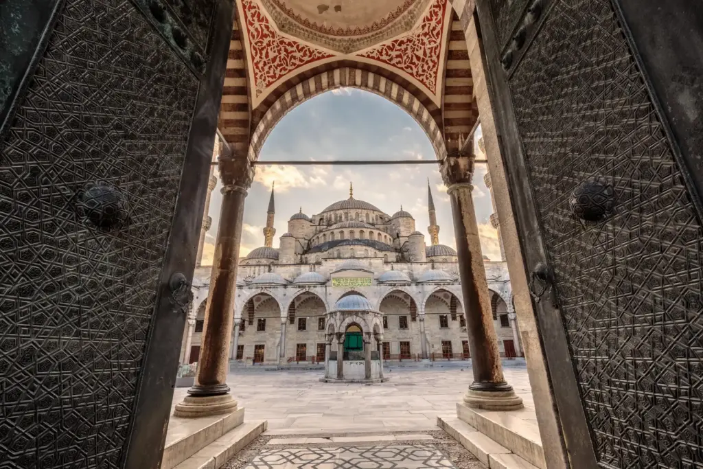 View of the Blue Mosque through the arched entrance of its inner courtyard, showing the central dome and minarets framed by Ottoman stonework