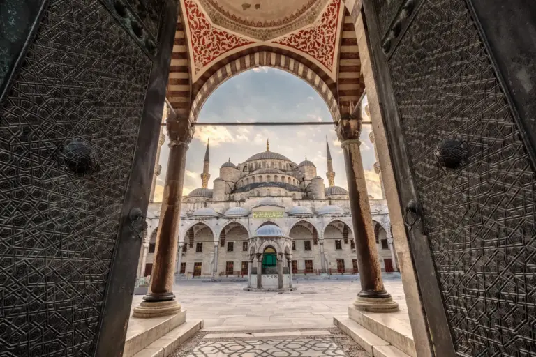 View of the Blue Mosque through the arched entrance of its inner courtyard, showing the central dome and minarets framed by Ottoman stonework