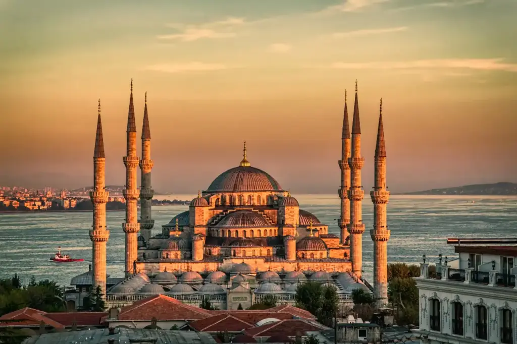 The Blue Mosque bathed in golden hour light with all six minarets, cascading domes, and the Sea of Marmara stretching behind it
