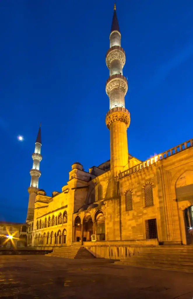 The Blue Mosque illuminated at night with golden floodlights highlighting the stone façade and minarets against a deep blue twilight sky