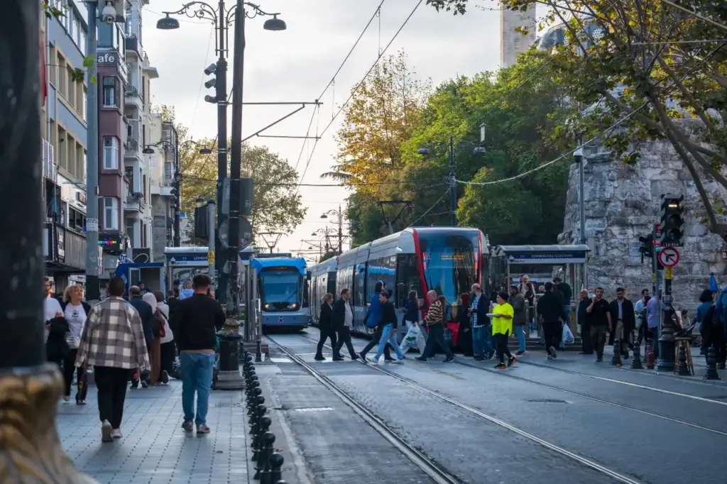 Istanbul T1 tram line near the Çemberlitaş stop with blue trams, pedestrians crossing the tracks, and the historic peninsula streetscape